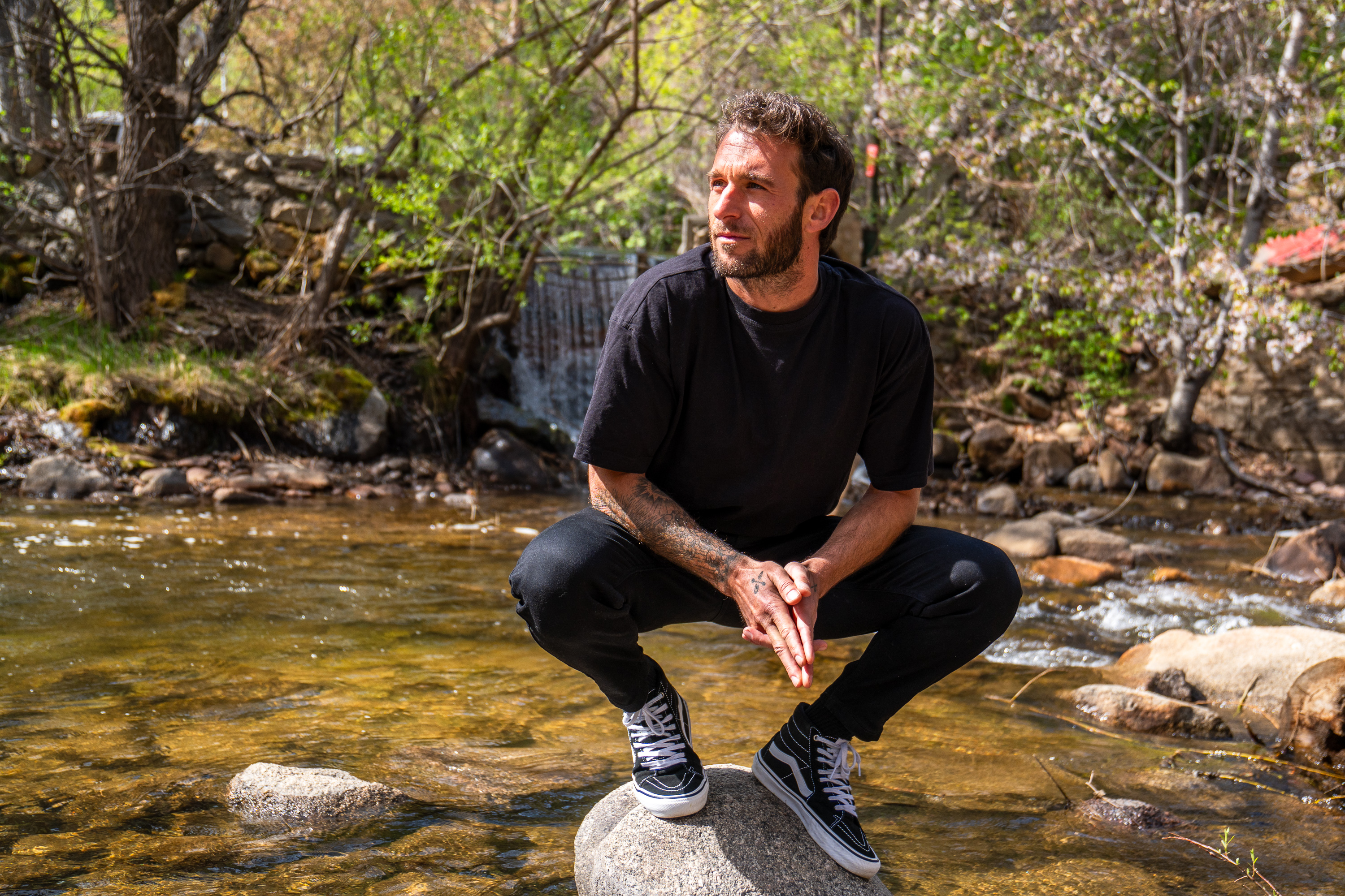 Nicholas Balsamo resting on a rock in the middle of a sunlit forest creek